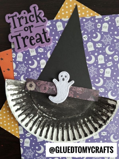 A paper plate witch hat painted black features a purple band and a white ghost cutout, set on Halloween-themed paper with spiderwebs, stars, and a "Trick or Treat" sign. @GLUETOMYCRAFTS is labeled below.