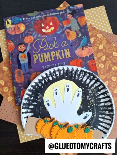 A children’s book titled “Pick a Pumpkin” by Patricia Toht is surrounded by autumn-themed paper and a festive pumpkin patch kid craft made from painted paper plates, a handprint ghost, and felt pumpkins. @GLUETOMYCRAFTS appears at the bottom.