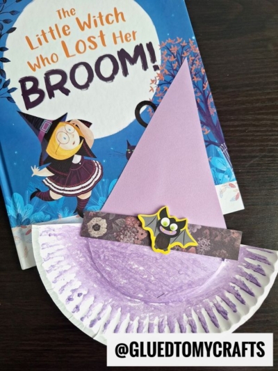 A children's book titled The Little Witch Who Lost Her Broom! is displayed beside a creative paper plate witch hat craft, made with pink paper and a bat sticker. The username @GLUEDTOMYCRAFTS appears at the bottom.