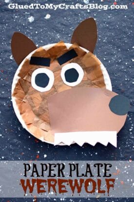 A paper plate werewolf face featuring brown paper patches, big ears, bold eyebrows, eyes, nose, and sharp white zigzag teeth on a speckled dark background. The text reads: Paper Plate Werewolf.
