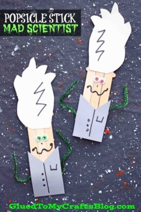 Two popsicle stick mad scientists with wild white hair, googly eyes, and pipe cleaner arms stand on a splattered dark background. “Popsicle Stick Mad Scientist” is boldly displayed at the top.