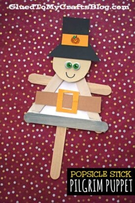 A popsicle stick pilgrim puppet craft featuring a black hat, googly eyes, paper belt, and a smile is displayed on a red background with yellow and white dots. Text reads: “POPSICLE STICK PILGRIM PUPPET.” Perfect for a pilgrim kid craft!.