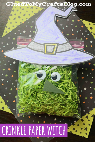 A crinkle paper witch, made from a plastic bag filled with green crinkle paper and topped with googly eyes, a paper nose, and a witch hat, sits on star-patterned paper. Text reads GluedToMyCraftsBlog.com and CRINKLE PAPER WITCH.
