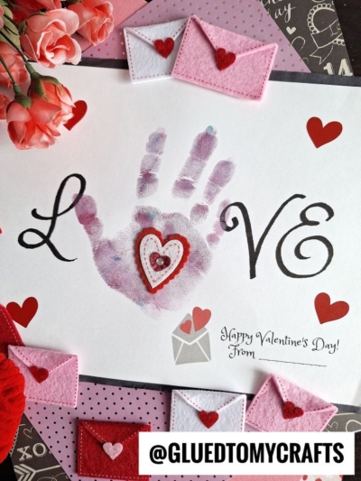 A sweet Valentine keepsake craft with “LOVE” in black, a pink handprint for the “O,” and layered felt hearts on the palm. Felt envelopes, red hearts, flowers, and @gluedtomycrafts handle complete this adorable handprint love keepsake.