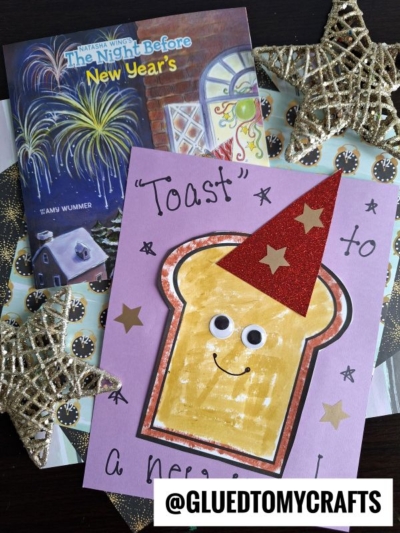 A handmade card reads “Toast To A New Year!” and features a smiling toast in a red glitter party hat, set beside The Night Before New Years book and gold star decorations—perfect for celebrating new beginnings.