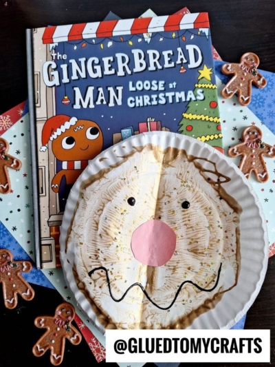 A children's book titled The Gingerbread Man Loose at Christmas is next to a paint splat gingerbread man paper plate craft, surrounded by small gingerbread cookies and a @GLUEDTOMYCRAFTS label at the bottom.