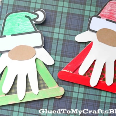 Craft Stick Christmas Gnomes made with paper, popsicle sticks, and handprint cutouts are displayed on plaid paper backgrounds