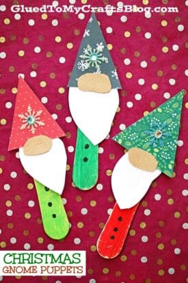 Three handmade Christmas gnome puppets, including a festive Christmas gnome scoop stick puppet, are crafted from painted sticks, paper, and embellishments and displayed on a red polka-dotted background. The text reads CHRISTMAS GNOME PUPPETS.