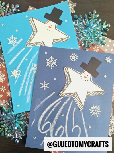 Two handmade winter cards feature snowman shooting star designs with black hats and drawn snowflakes on blue paper backgrounds, surrounded by decorative snowflakes. @GLUEDTOMYCRAFTS is written in the corner.