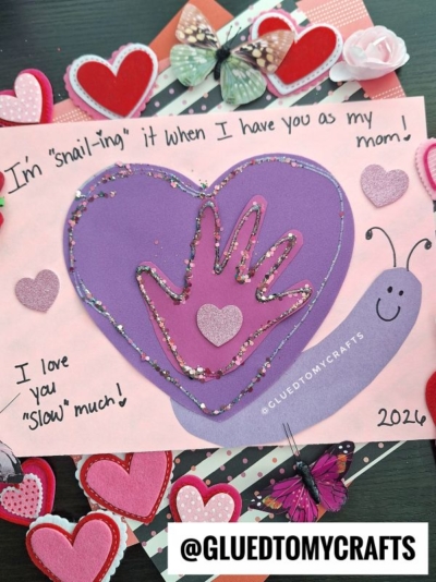 A handmade Valentine’s Day card features a handprint inside a large purple heart, decorated with glitter. This adorable heart valentine snail card reads, I’m snail-ing it when I have you as my mom! I love you slow much!.