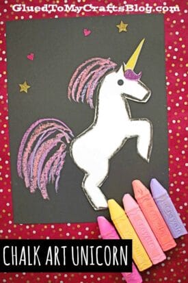 A drawing of a white paper & chalk unicorn with a yellow horn and purple mane and tail, outlined in black on black paper. Pink, purple, and yellow chalk pieces are nearby. The red background shines with gold stars. Text reads CHALK ART UNICORN.