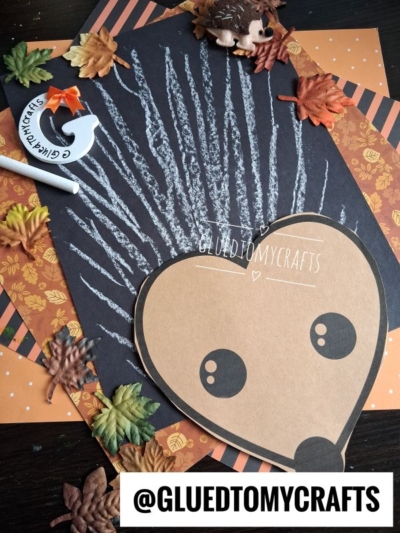 A charming porcupine craft featuring a paper face and white chalk art spines on black paper, surrounded by fall leaves, an acorn, a marker, and a small chalk art hedgehog figure. The text @GLUEDTOMYCRAFTS is at the bottom.