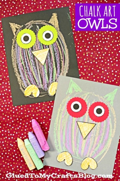Two colorful owl drawings made with chalk and paper cutouts, displayed on black and gray paper with four pastel chalk sticks on a red polka dot background. This charming chalk art owl craft features text that reads “Chalk Art Owls” and “GluedToMyCraftsBlog.com.”.