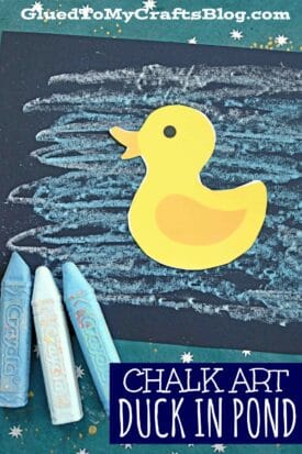 A yellow paper duck is placed on a dark background with blue and white chalk lines resembling water. Three pastel Crayola chalk pieces are on the left. Text reads Chalk Art Duck in Pond—perfect for a fun duck pond craft.