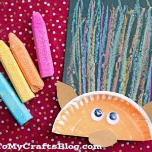 A children’s troll craft made with a paper plate for the face, googly eyes, colored paper ears, and fun chalk art hair, next to four large pastel crayons on a red polka dot background. GluedToMyCraftsBlog.com text is at the bottom.