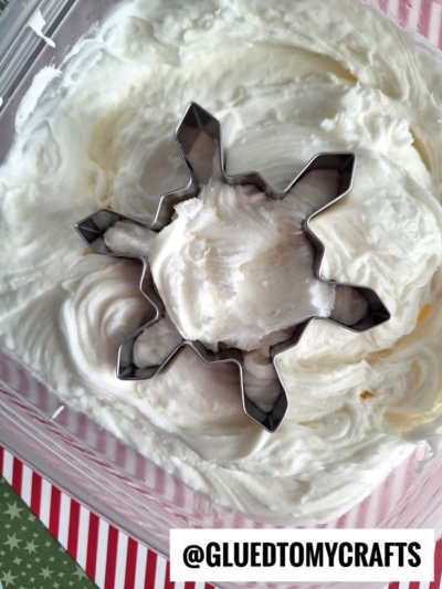 A metal snowflake-shaped cookie cutter is pressed into a container of white moon dough slime. A striped red and white paper and the text @GLUEDTOMYCRAFTS appear at the bottom of the image.