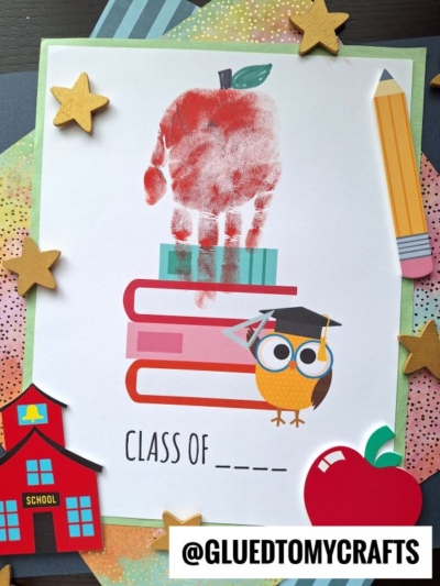 A handprint forms a vibrant red apple on top of stacked books, with an owl in a graduation cap perched beside it. “Handprint Class of ____” is written below. The art is decorated with stars, a pencil, and a schoolhouse.