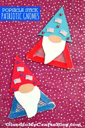 Two popsicle stick patriotic gnome crafts sit on a red polka dot background—one with a blue hat and mini American flags, the other with a red hat and flags. Both feature white beards and GluedToMyCraftsBlog.com at the bottom.
