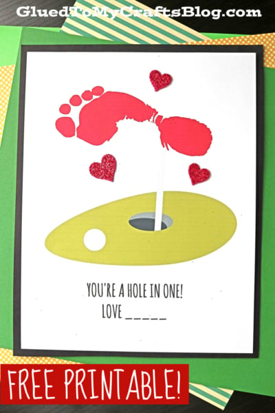 A craft card features a red footprint forming a golf club and ball above a green footprint hole in one, surrounded by red glitter hearts. Text below reads, Youre a hole in one! Love _____. FREE PRINTABLE! appears at the bottom.