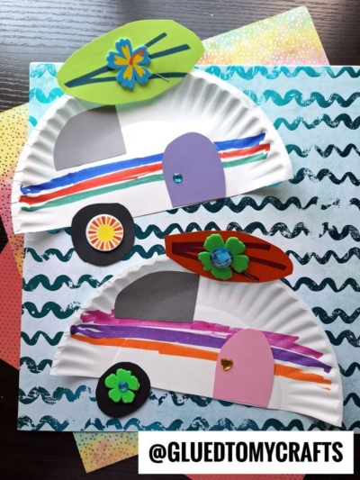 Two paper plate beach campers resemble camper vans with surfboards on top, decorated with colorful markers, cut-out shapes, and flower embellishments, displayed on patterned paper. @GLUEDTOMYCRAFTS is written at the bottom.