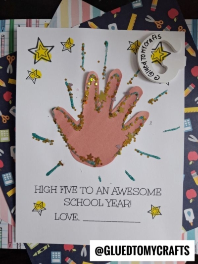 A craft card featuring a cut-out handprint high five decorated with glitter and stars, with the message High five to an awesome school year! Love, ______. @GLUETOMYCRAFTS is noted at the bottom.