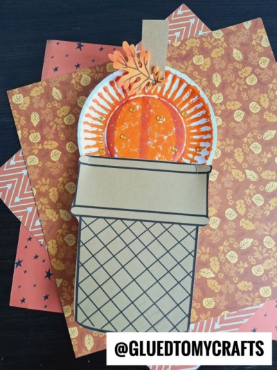 A handmade Olympic torch craft made from a paper plate, colored paper, and orange tissue to resemble flames, placed on autumn-themed patterned paper—perfect alongside a paper plate pumpkin or ice cream craft. @GLUEDTOMYCRAFTS is written at the bottom.