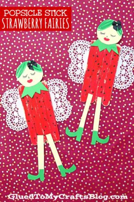 Two Strawberry Fairy popsicle stick crafts with green paper hair, red outfits like strawberries, green collars and shoes, paper wings, and closed eyes are set against a pink polka dot background.