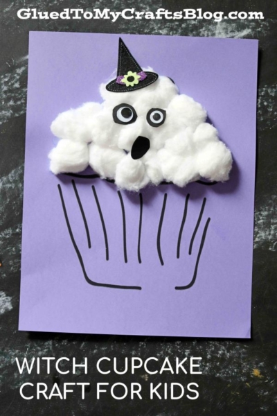 A kids’ craft of a witch cupcake made from cotton balls on purple paper, inspired by the popular cotton ball ghost cupcake project, with googly eyes, a small black hat, a black mouth, and black lines for the cupcake base.