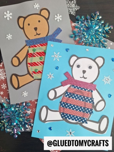 Two handmade teddy bear crafts on colored paper wear patterned sweaters and scarves. One is a washi tape bear in sweater style on gray; the other is white with googly eyes on blue. Snowflake and heart decorations surround them. @GLUEDTOMYCRAFTS is at the bottom.
