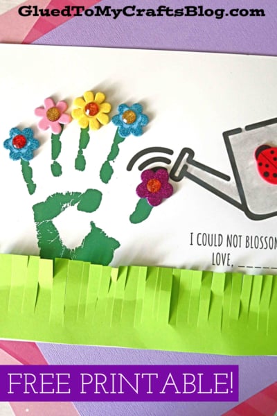 A craft project featuring a green handprint as flower stems, colorful flower stickers at the fingertips, a paper watering can, green paper grass fringe, and cheerful text: FREE PRINTABLE! and "I could not blossom without you.