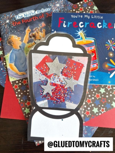 A gumball machine craft with red, white, and blue stars and glitter sits atop patriotic-themed children’s books, star-patterned paper, and a colorful paper camping lantern. The Instagram handle @GLUEDTOMYCRAFTS is displayed at the bottom.
