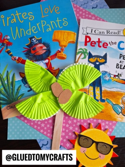Two children’s books, Pirates Love Underpants and Pete the Cat, are on patterned paper. A green cupcake liner flower craft, a cupcake liner palm tree, and a smiling sun with sunglasses complete the scene. Text reads @GLUEDTOMYCRAFTS.
