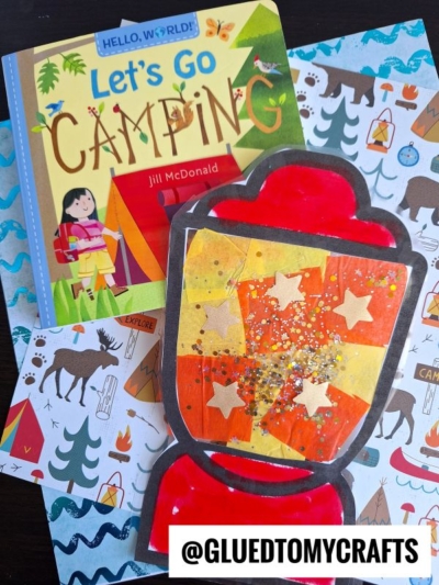 A children’s book titled “Let’s Go Camping” sits next to colorful camping-themed scrapbook paper and a stained glass camping lantern craft with yellow stars and glitter. The @gluedtomycrafts watermark is at the bottom.
