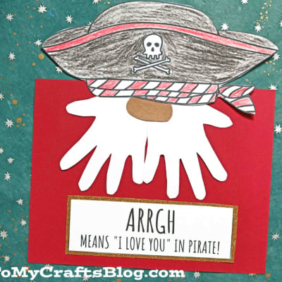 A handmade pirate handprint craft features a paper pirate hat, red and white scarf, and a white handprint beard on a red background. Text reads: “ARRGH means ‘I love you’ in pirate!” and “Handprint Pirate Gnome.”.