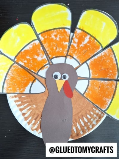 A paper plate candy corn turkey craft with painted yellow and orange feather cutouts and a brown paper body.