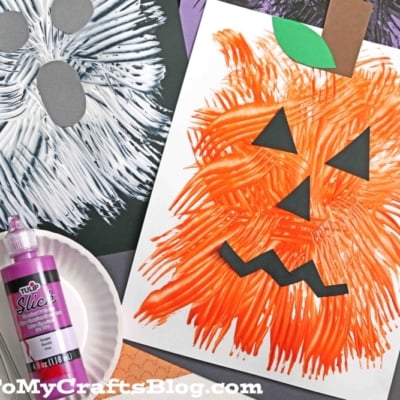 A white ghost and an orange pumpkin are fork painted on paper, creating a fun fork painted Halloween craft. The pumpkin features black paper eyes, nose, and mouth with a green stem. A purple paint bottle and a paper plate with a fork sit nearby.