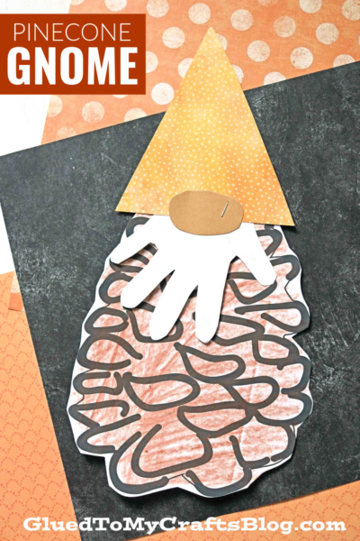 A handmade pine cone gnome crafted from cut-out paper shapes, featuring a textured pinecone body, white handprint beard, peach oval nose, and orange polka-dot hat. The background is decorated with patterned papers for extra charm.