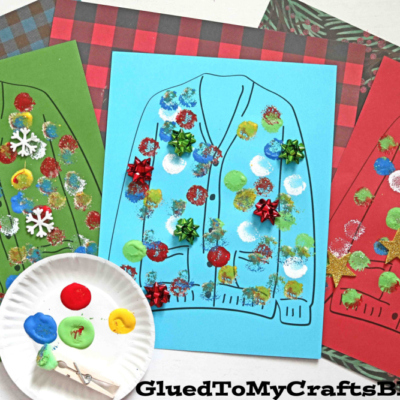 Three pieces of colored paper feature polka dot ugly sweater outlines decorated with paint, glitter, stickers, and bows. A paper plate with blotches of paint and a clothespin is in the foreground. GluedToMyCraftsBlog.com is at the bottom.