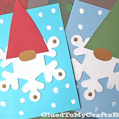 Two handmade craft foam snowflake gnome crafts on colored paper backgrounds, each with a large white snowflake body, red or green pointed hat, beige oval nose, and scattered white and gold dots.