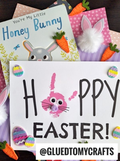 Easter-themed crafts with a bunny book, handprint "Hoppy Easter!" card featuring a pink bunny face as the “O,” googly eyes, pom-poms, felt carrots, eggs, and bunny ears on a pink polka dot background.