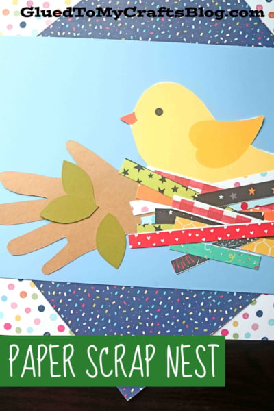 A kids’ craft of a yellow paper bird in a colorful paper bird’s nest, made from paper scraps and a brown handprint cutout, on a blue polka dot background. Text reads PAPER SCRAP NEST.