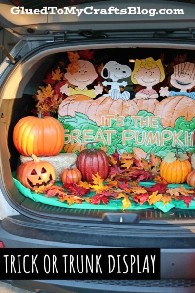 A car trunk decorated with pumpkins, autumn leaves, and Peanuts characters for Halloween. The backdrop reads “It’s The Great Pumpkin.” Perfect for a Great Pumpkin trick or trunk display! Text on photo: “TRICK OR TRUNK DISPLAY.”.