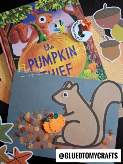 Childrens book The Pumpkin Thief with an autumn-themed squirrel on tree branch craft, made from paper cutouts, paint dots as acorns, a foam pumpkin, and decorative acorn and leaf shapes. Handle @GLUEDTOMYCRAFTS is shown.