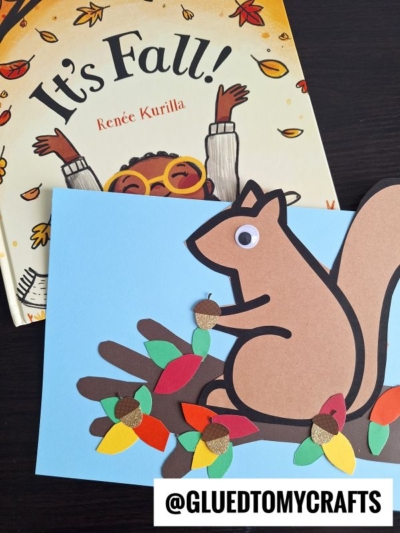 A childrens book titled Its Fall! by Renée Kurilla is next to a squirrel on tree branch craft made of paper, featuring colorful leaves and small acorns. The squirrel has a googly eye and sits on a blue background. @GLUEDTOMYCRAFTS is at the bottom.