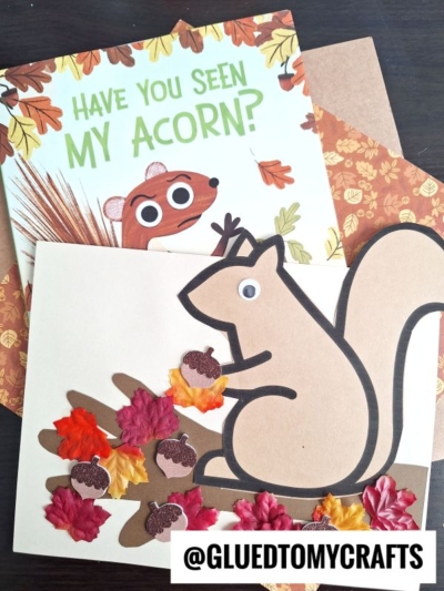 A children’s book titled Have You Seen My Acorn? with a squirrel illustration is next to a squirrel on tree branch craft made from paper, artificial leaves, and paper acorns. The @GLUEDTOMYCRAFTS handle is at the bottom.