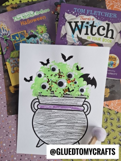 A Halloween-themed craft scene shows a pom pom stamped cauldron filled with green, bubbly potion, googly eyes, and black bat cutouts. Two Halloween books are in the background. The handle @GLUEDTOMYCRAFTS is at the bottom.
