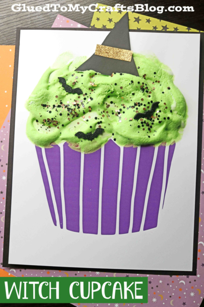 A craft of a witch cupcake with green frosting, purple wrapper, black bat confetti, glitter, and a small black witch hat on top. The text at the bottom reads WITCH CUPCAKE. Perfect inspiration for your next puffy paint witch cupcake project!.