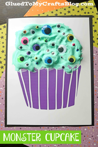 A craft project of a puffy paint monster cupcake with green, fluffy frosting topped with colorful googly eyes on a purple cupcake liner, displayed on a star-patterned background. Text reads MONSTER CUPCAKE.