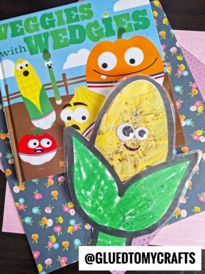 A children’s book titled Veggies with Wedgies featuring cartoon vegetables and a homemade stained glass corn craft with googly eyes and glitter, all on a floral background. Text at bottom: @GLUEDTOMYCRAFTS.
