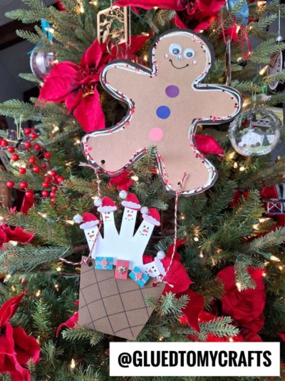 A decorated Christmas tree with red poinsettias, featuring a gingerbread man hot air balloon and a paper craft of Santa and reindeer in a chimney, with the text @GLUETOMYCRAFTS at the bottom.